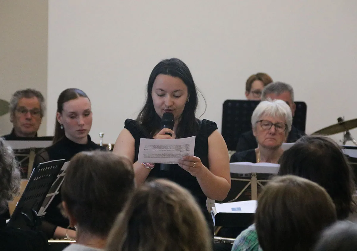 Conteuse lisant son texte au premier plan devant les musiciens — concert de printemps du 9 mai 2026 à Uxegney