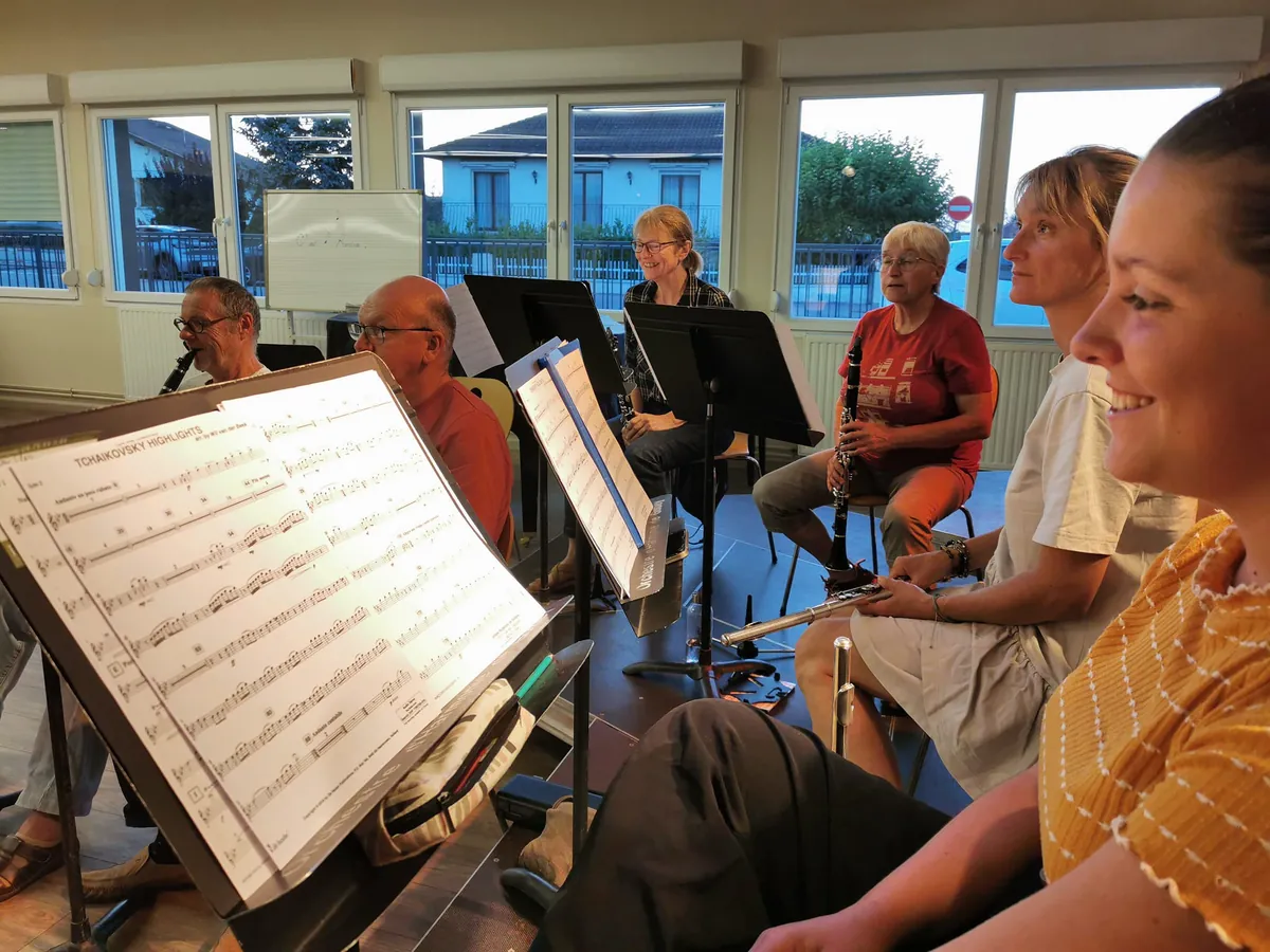 Une musicienne assise près de son pupitre avec l’orchestre en répétition à l’arrière-plan